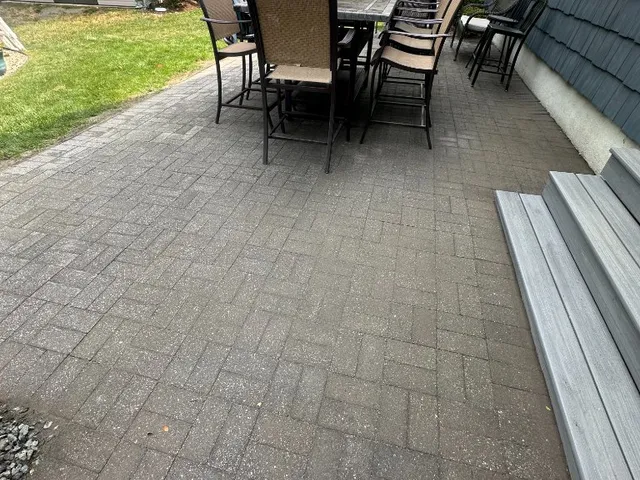 Backyard paver patio with dining set beside a gray composite deck and shingle siding