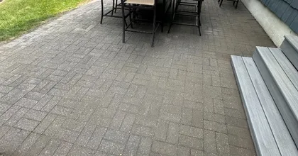 Backyard paver patio with dining set beside a gray composite deck and shingle siding