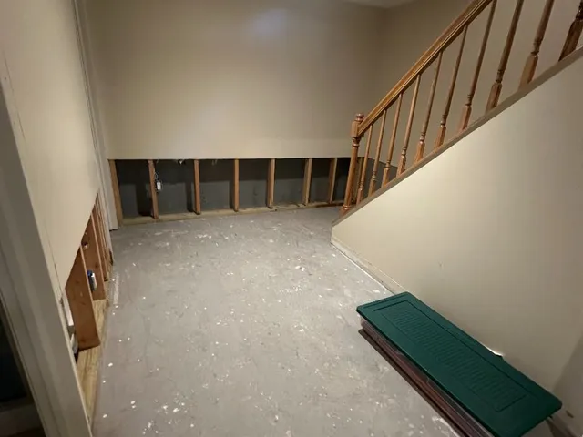 Unfinished basement with exposed wall framing and wooden staircase before drywall