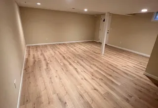 Newly painted tan basement room with recessed lighting and laminate floor
