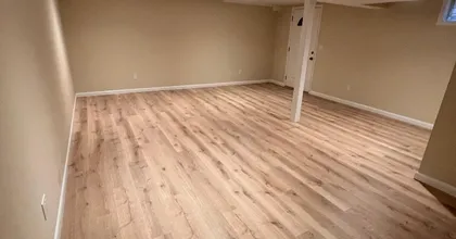 Newly painted tan basement room with recessed lighting and laminate floor