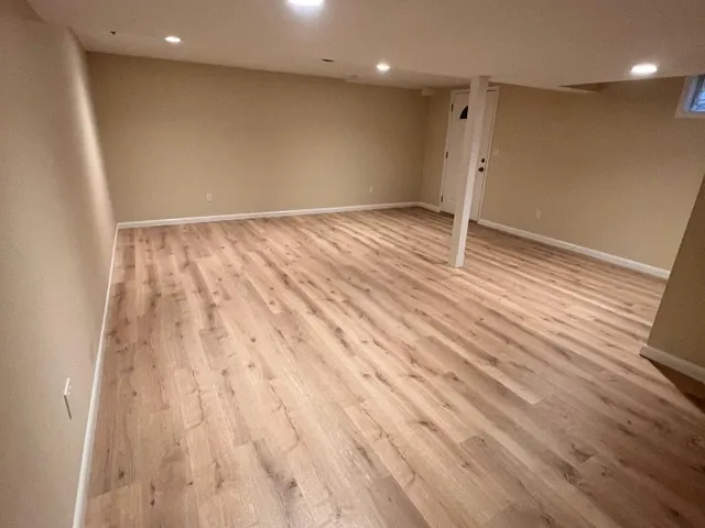 Newly painted tan basement room with recessed lighting and laminate floor
