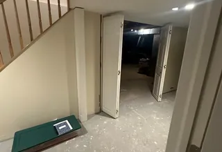 Painted basement landing with white bi-fold doors under a wood staircase