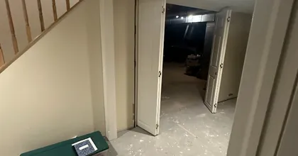 Painted basement landing with white bi-fold doors under a wood staircase