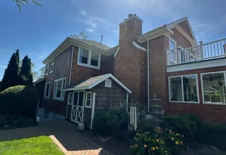 Two-story cedar shingle home with brick chimney and paver walkway in summer