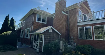 Two-story cedar shingle home with brick chimney and paver walkway in summer