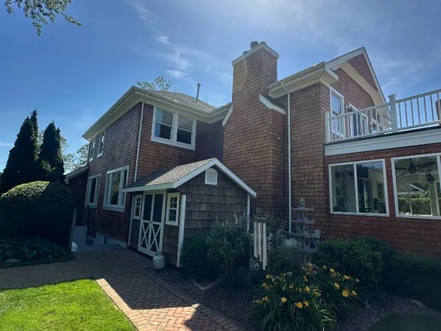 Two-story cedar shingle home with brick chimney and paver walkway in summer
