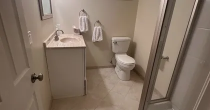 Freshly painted beige basement bathroom with vanity, toilet and glass shower